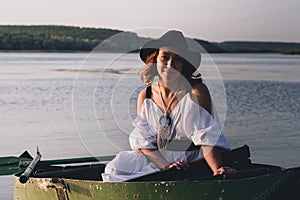 Happy bride in black hat in a boat on the river