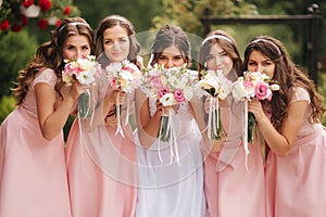 Happy bride with bridesmaid hold bouquets and have fun outside. Beautiful bridesmaid in same dresses stand by the