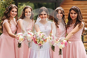 Happy bride with bridesmaid hold bouquets and have fun outside. Beautiful bridesmaid in same dresses stand by the