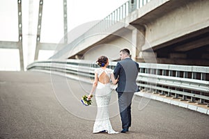 Happy bride and groom celebrating wedding day. Married couple going away on bridge. Long family life road concept.