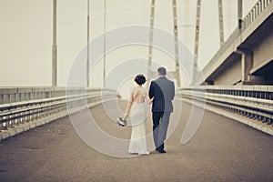 Happy bride and groom celebrating wedding day. Married couple going away on bridge. Long family life road concept. Toned