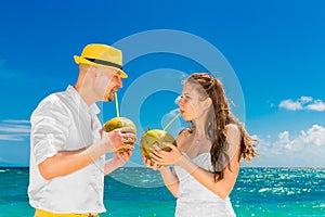 Happy bride and groom drink coconut water on a tropical beach. W