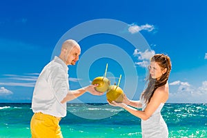 Happy bride and groom drink coconut water on a tropical beach. W