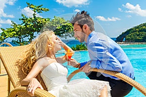 Happy bride and groom enjoy a cocktail poolside infinity. Tropic