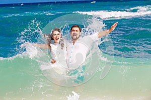 Happy bride and groom having fun in the waves on a tropical beach. Wedding and honeymoon on the tropical island.