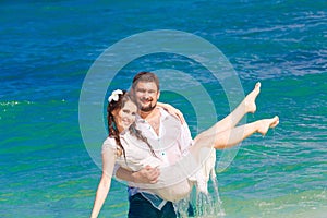 Happy bride and groom having fun in the waves on a tropical beach. Wedding and honeymoon on the tropical island.