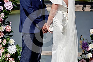 Happy bride and groom holding hands on wedding ceremony, copy space. Wedding couple in love, newlyweds. Bridal bouquet.