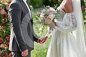 Happy bride and groom holding hands on wedding ceremony, copy space. Wedding couple in love, newlyweds. Bridal bouquet.