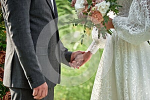 Happy bride and groom holding hands on wedding ceremony, copy space. Wedding couple in love, newlyweds. Bridal bouquet.