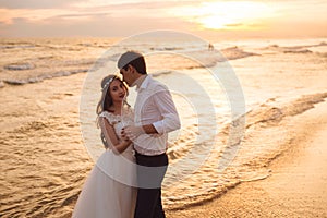 Happy bride and groom hugging on ocean beach at sunset time. Romantic couple newlyweds on their wedding day.