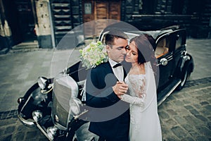 stylish bride and groom sensually posing near retro car with boh