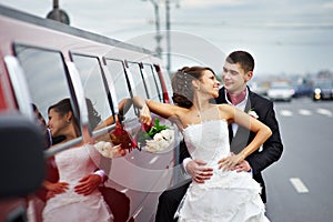 Happy bride and groom near wedding limo