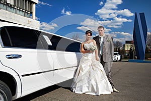 Happy bride and groom near wedding limo