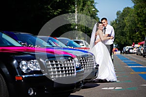 Happy bride and groom near wedding limousines