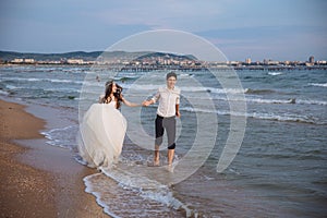 Happy bride and groom run along ocean shore. Newlyweds having fun at wedding day on tropical beach