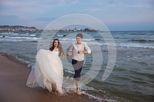 Happy bride and groom run along ocean shore. Newlyweds having fun at wedding day on tropical beach