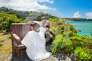 Happy bride and groom sitting on the bench in front of beautiful