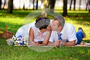 Happy bride and groom on their wedding lies on the grass in park and kiss