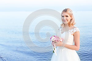 Happy bride holding wedding bouquet on beach.