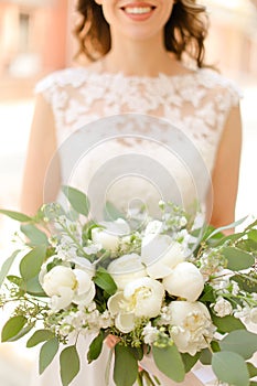 Happy bride keeping bouquet of flowers and wearing white dress.