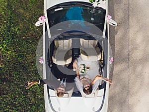 Happy bride kiss groom, newlywed wedding couple is driving a convertible retro car with balloons on a country road for