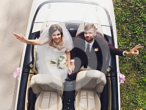 Happy bride kiss groom, newlywed wedding couple is driving a convertible retro car with balloons on a country road for