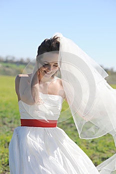 Happy bride in white dress walking on green field