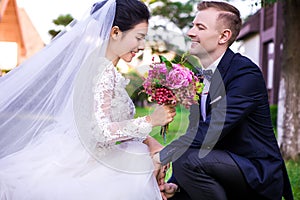 Happy bridegroom looking at beautiful bride holding bouquet outdoors