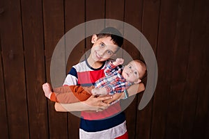 Happy brother holding a newborn baby boy in his arms on the brown background. Brothers, family, friends. Newborn photosession. Bab