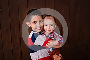 Happy brother holding a newborn baby boy in his arms on the brown background. Brothers, family, friends. Newborn photosession. Bab