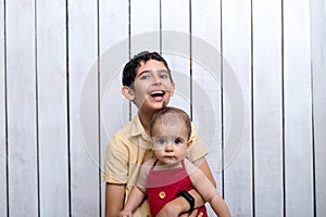 Happy brother holding a newborn baby boy in his arms on the white background. Brothers, family, friends. Newborn photosession.