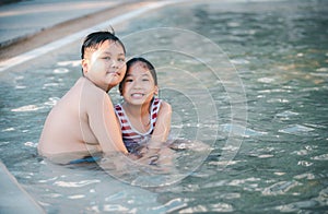 Happy brother and sisiter are playing water at swimming pool