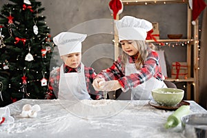 Happy brother and sister cooking Christmas gingerbread in the kitchen, cookie dough, little chefs preparing food.