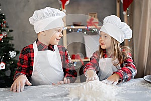 Happy brother sister make dough for Christmas cookies, children in the kitchen are preparing gingerbread cookies, little