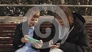 happy brother and sister sitting on a bench in the park holding phones in their hands, children