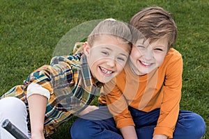 Happy brother and sister sitting together on green grass and smiling at camera