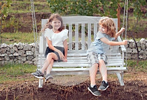 Happy brother and sister swinging on swing in summer park outdoors. Little boy and girl kids enjoying summer. Kids