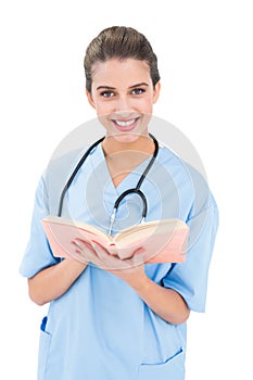 Happy brown haired nurse in blue scrubs holding a book