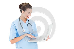 Happy brown haired nurse in blue scrubs using a laptop