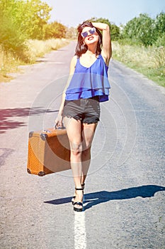 Happy Brunette beautiful girl traveler with suitcase on road, hitchhiking. Concept of travel, adventure, vacation, freedom. Waitin