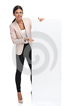 Happy brunette female in pink jacket recommending empty board