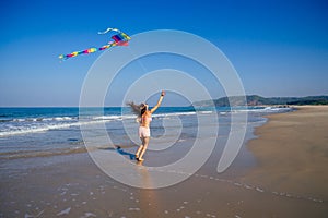 Happy brunette girl in a bathing suit and short pink playing with flying kite on tropical beach copyspase