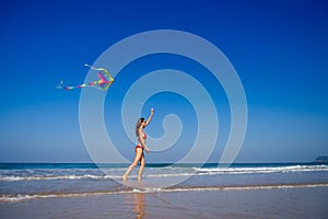 Happy brunette girl in a bathing suit and short pink playing with flying kite on tropical beach copyspase hills and