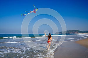 Happy brunette girl in a bathing suit and short pink playing with flying kite on tropical beach copyspase hills and