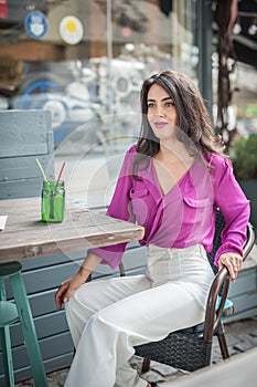 Happy Brunette Girl with pink blouse Sitting at the bar , Drinking a glass of lemonade While Smiling at the camera.