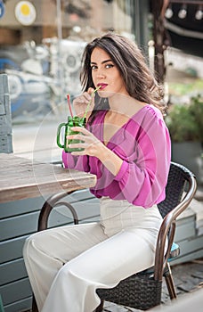 Happy Brunette Girl with pink blouse Sitting at the bar , Drinking a glass of lemonade While Smiling at the camera.