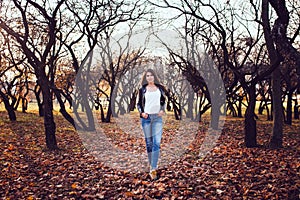 Happy brunette in jeans and leather jacket in an apple orchard on a walk is an energetic successful woman