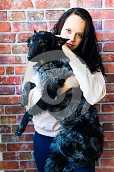 Happy brunette lady in casual wear hugging mudi pet dog, studio background.