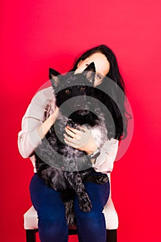 Happy brunette lady in casual wear hugging mudi pet dog, studio background.