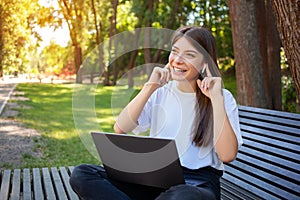 Happy brunette student girl sitting on bench in park with laptop